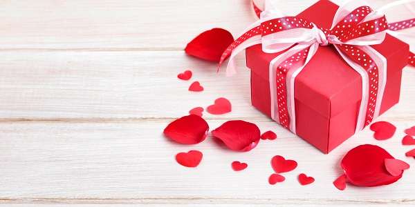 Valentine background of gift box and rose petals on white wood. Space for copy.