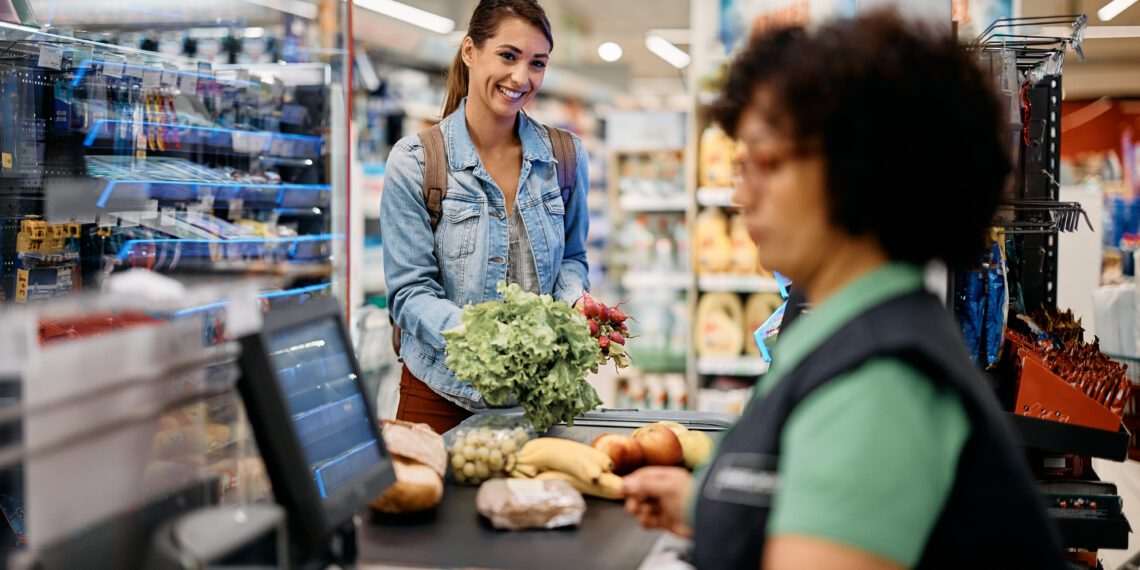 Young happy woman paying for groceries at checkout in supermarket.